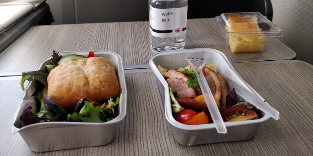 PICTURE OF THE BOXED LUNCH, PLASTIC CUTLERY, AND BOTTLE OF WATER FOR THE MEAL IN BUSINESS CLASS WHILE FLYING THE COOP.