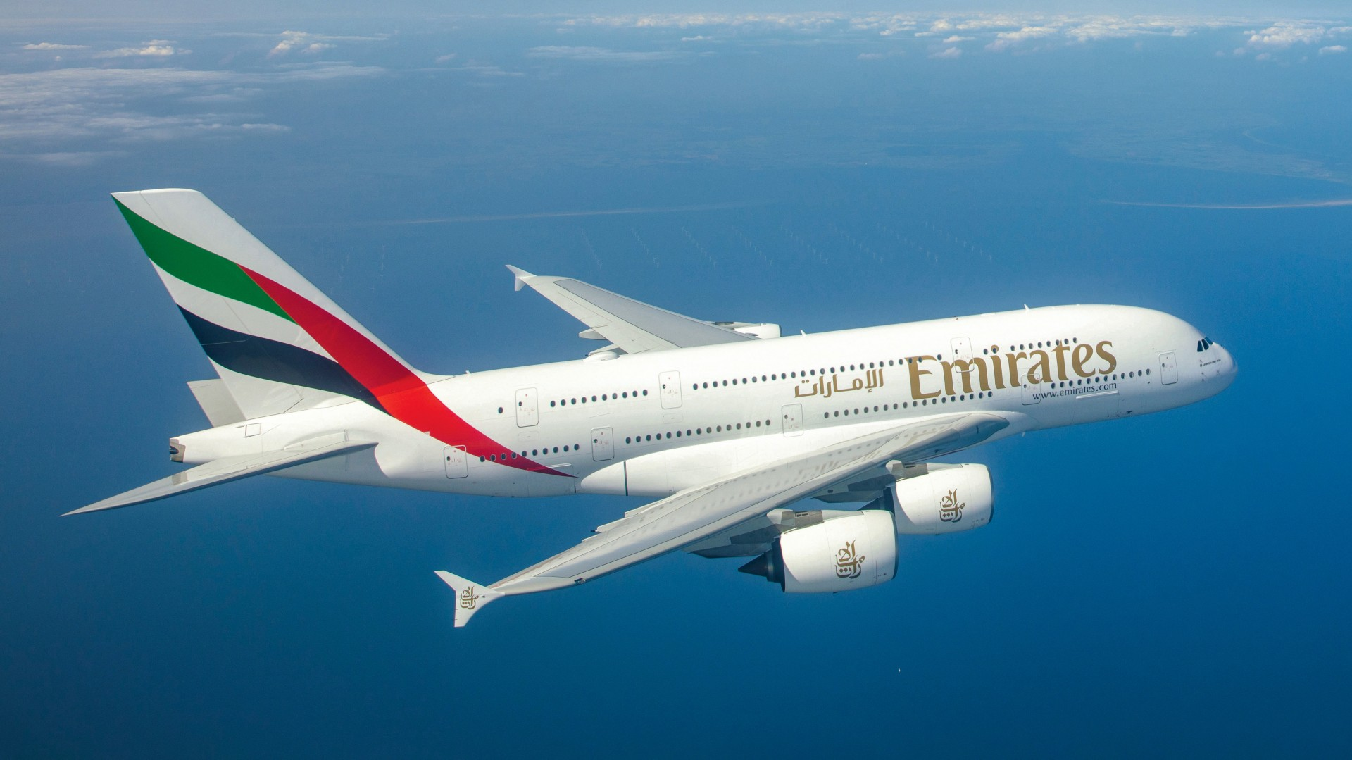 PICTURE OF AN EMIRATES A380 IN THE SKY OVER THE WATER.