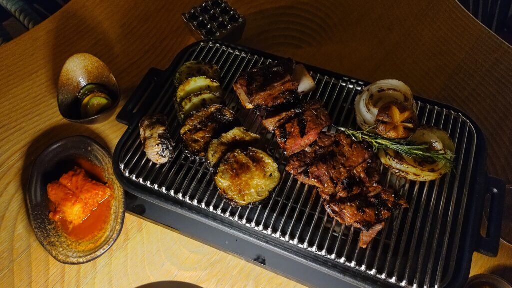 PICTURE OF THE BEEF SERVED ON A GRILL WITH A SIDE OF KIMCHI AND VEGETABLES.